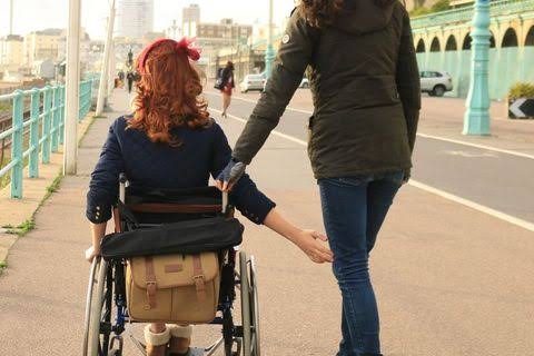 Woman on a skateboard pushes a woman in a wheel chair