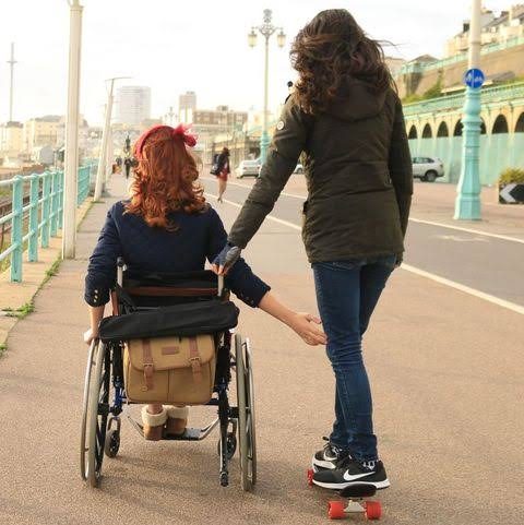 Woman on a skateboard pushes a woman in a wheel chair