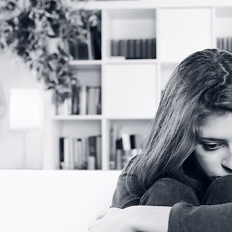 young woman sitting on sofa looking sad while mother looks at her worried