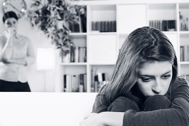 young woman sitting on sofa looking sad while mother looks at her worried