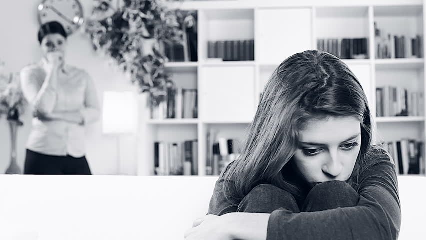 young woman sitting on sofa looking sad while mother looks at her worried