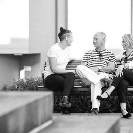 Black and white picture of 3 people sitting on a bench talking
