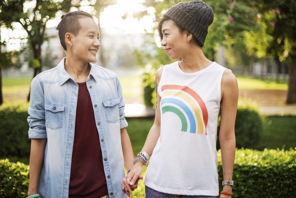 2 asian women holding hands in park and smiling 