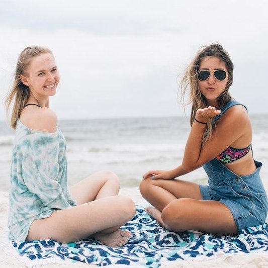 2 young women sitting on a beach