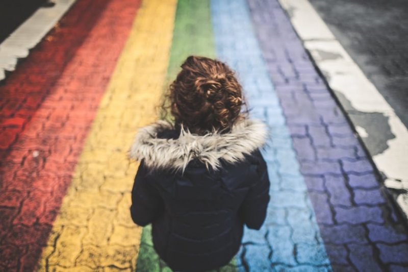 young woman from behing walking along a rainbow coloured path 