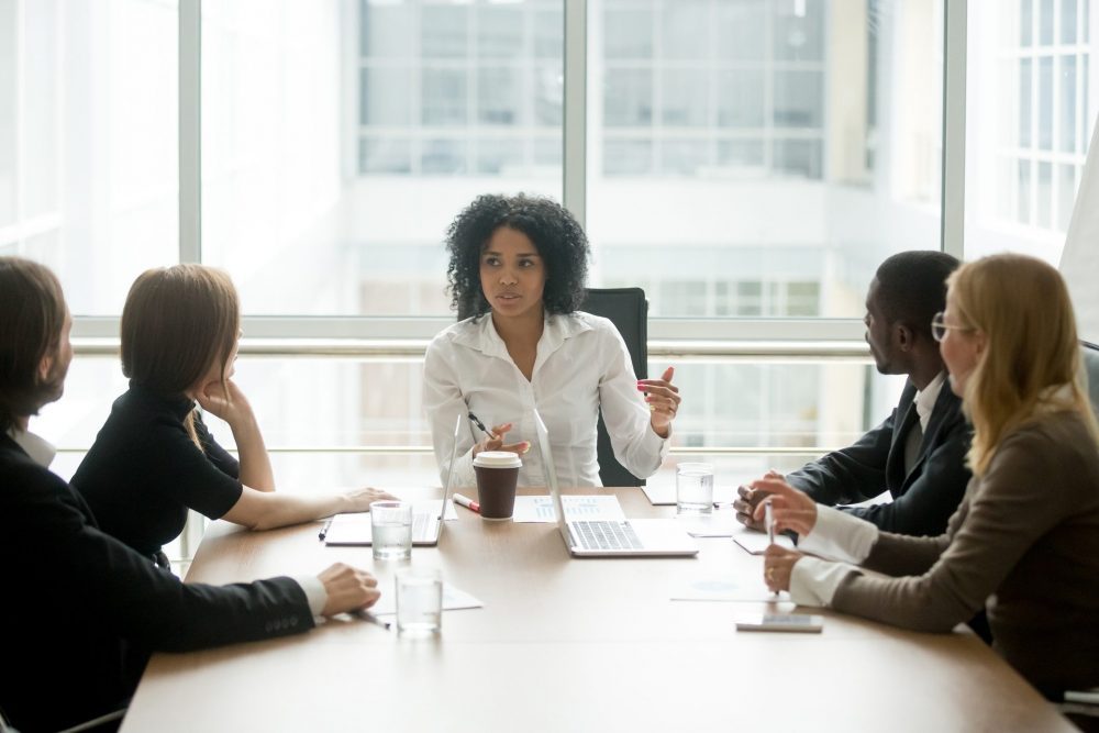 Woman of colour sitting at head of boardroom table talking