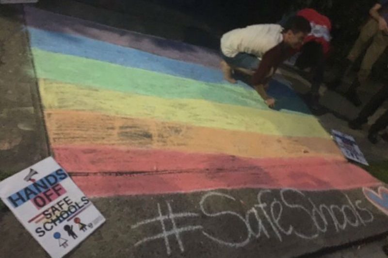 Person chalking Rainbow flag on footpath
