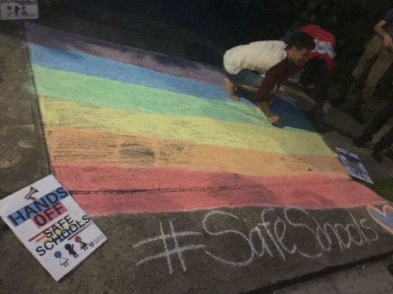 Person chalking Rainbow flag on footpath
