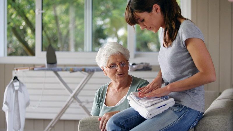 A younger woman folding laundry for an older woman