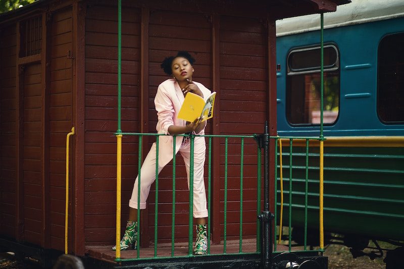black woman reading book next to a train
