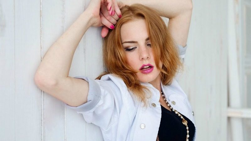 young woman with red hair leaning against white fence