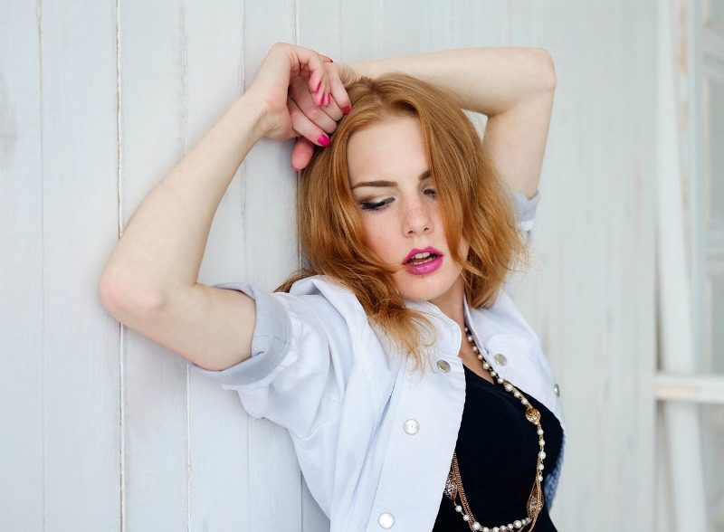young woman with red hair leaning against white fence