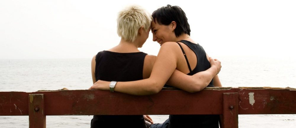 2 women sitting on bench by the water