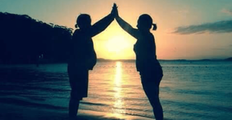 two women sillouettes holding hands up on beach