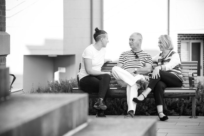 Black and white picture of 3 people sitting on a bench talking 