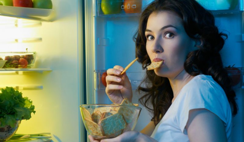 Woman eating crackers in front of fridge