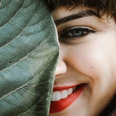 smiling women looking from behind large leaf