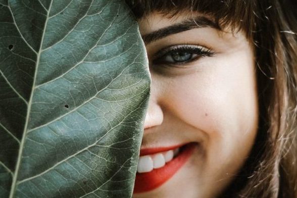 smiling women looking from behind large leaf