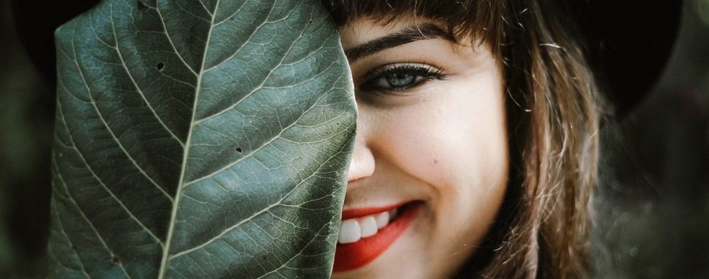 smiling women looking from behind large leaf