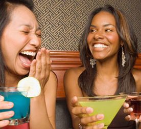 2 young women laughing over cocktails 