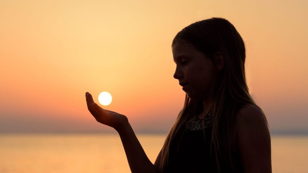 young woman holding the sun in her palm