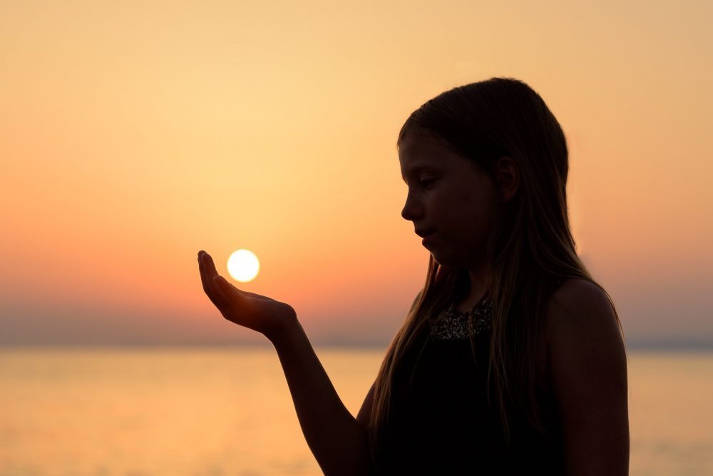 young woman holding the sun in her palm