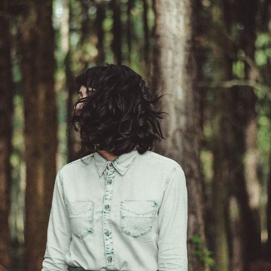 Young woman standing in forest with hair covering her face